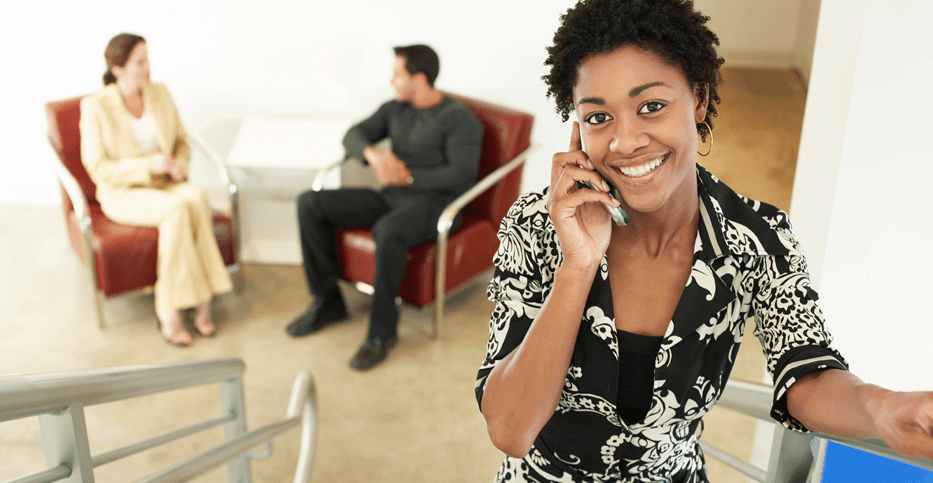 businesswoman negotiates on her phone while two clients patiently wait in the background